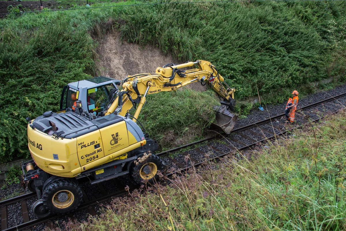 Gleisbagger und Arbeiter stehen auf einem Bahngleis.